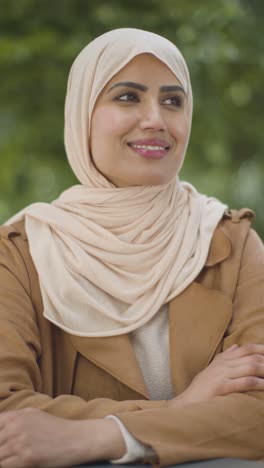 Vertical-Video-Portrait-Of-Smiling-Muslim-Woman-Wearing-Hijab-Sitting-At-Outdoor-Table-On-City-Street